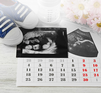 Kalender mit Ultraschallbild und Babyschuhen auf Holztisch