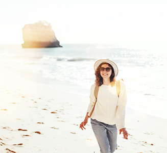 Frau mit Hut und Rucksack läuft am Strand mit Felsen