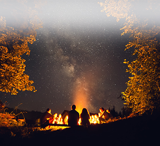 Gruppe von Personen um Lagerfeuer bei Nacht mit Sternenhimmel